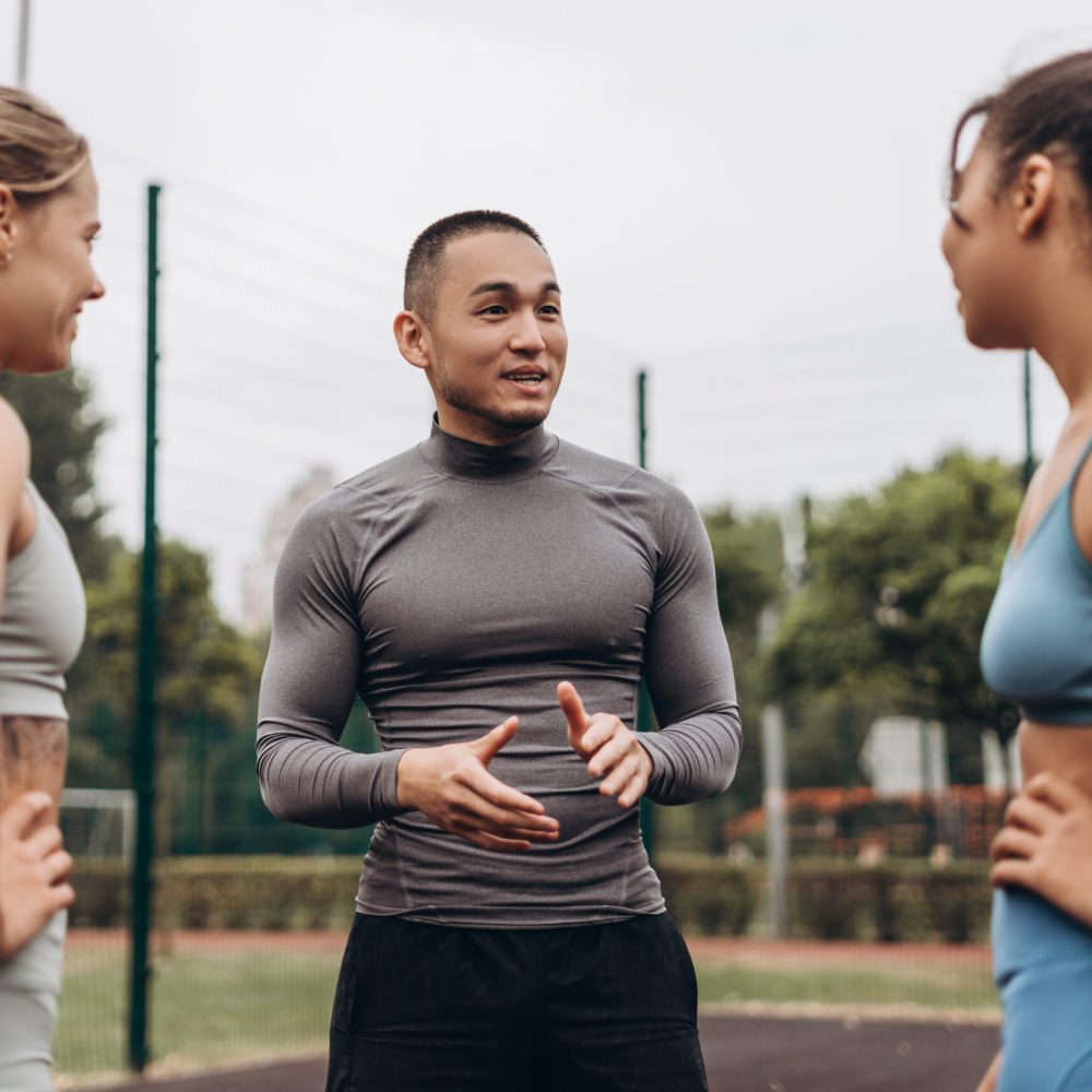 Group of happy, multinational women and man wearing stylish sportwear, talking, training together on the street, outdoors. Teamwork concept